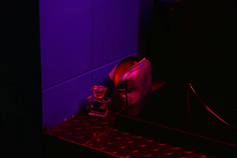 a bag sitting on top of a table in a dark room, a still life, inspired by Nan Goldin, unsplash, holography, purple leather dungeon bedroom, stage at a club, perfume, blue and red lighting