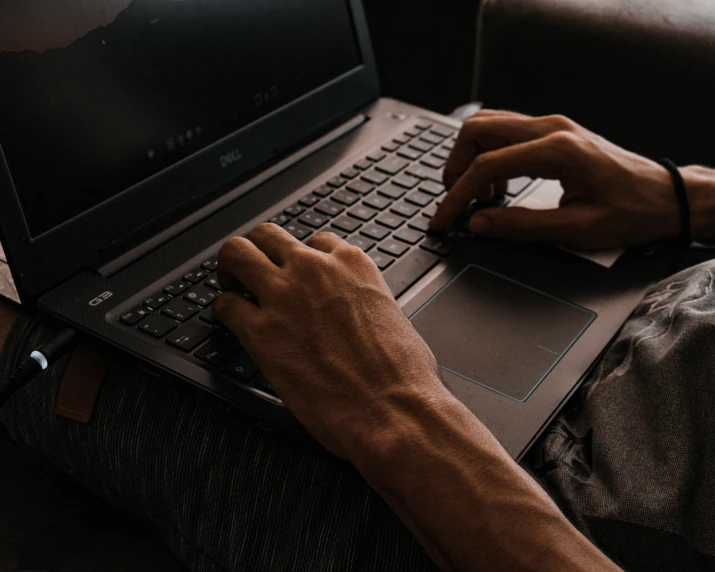 a man sitting on a couch using a laptop computer, trending on pexels, bottom angle, brown, intricate detailing, gaming computers