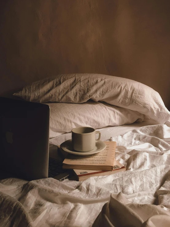 a laptop computer sitting on top of a bed next to a coffee cup