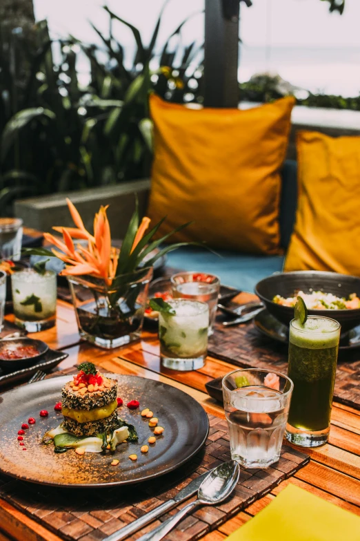 a wooden table topped with plates of food, by Julia Pishtar, bali, colorful coctail, lounge, harvest