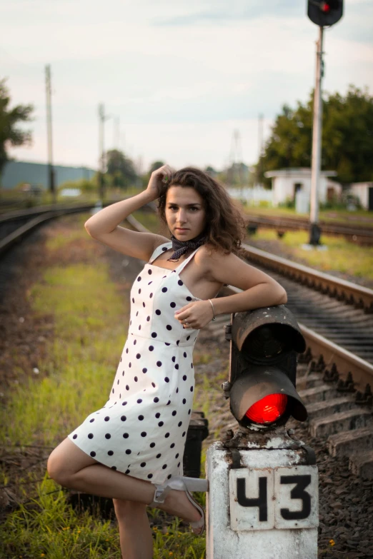 woman in dress leaning on train tracks in a rural setting