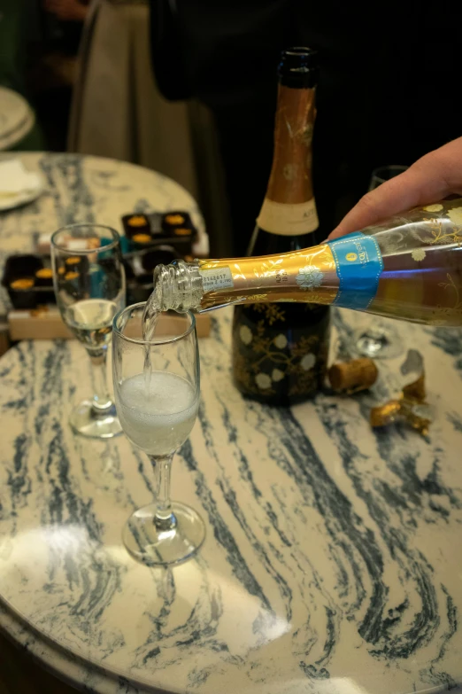 a person pouring a bottle of champagne into a glass, blue and white and gold, slide show, square, resin