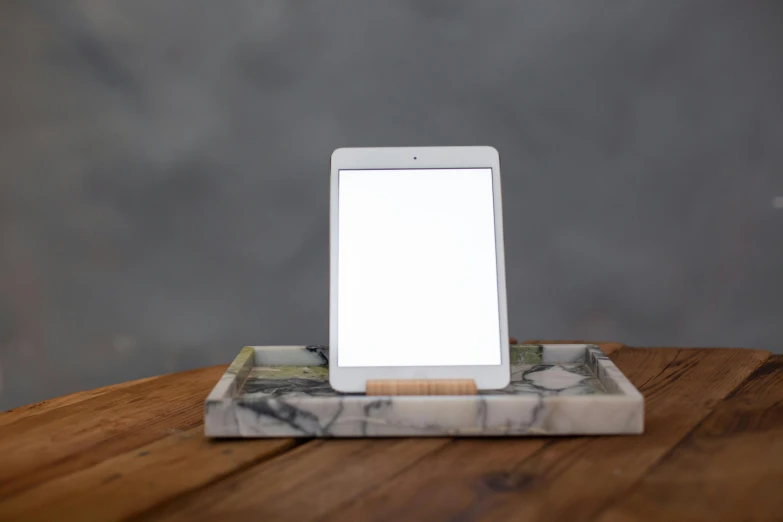 a tablet computer sitting on top of a wooden table, a portrait, by Jessie Algie, light and space, carrara marble, square, medium lighting, slate