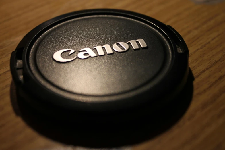 a canon lens cap sitting on top of a wooden table, a picture, by Tom Carapic, unsplash, photorealism, photograph credit: ap, on black background, close up high detailed, metal lid