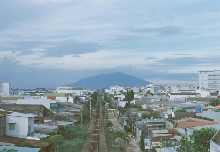 a train traveling down train tracks next to a city, by Carey Morris, sumatraism, full frame image, seaview, fujicolor photo, high quality image