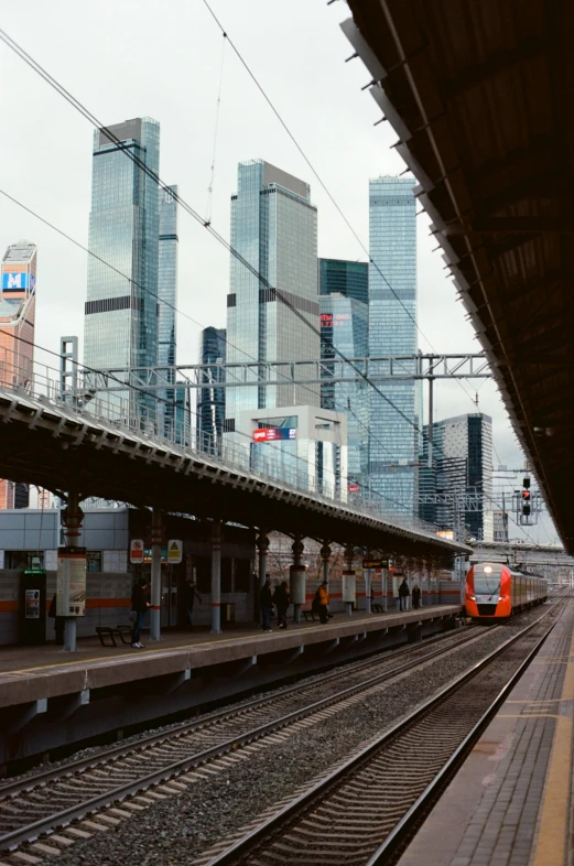 a train pulling into a train station next to tall buildings, russia in 2 0 2 1, square, 2022 photograph, orange line