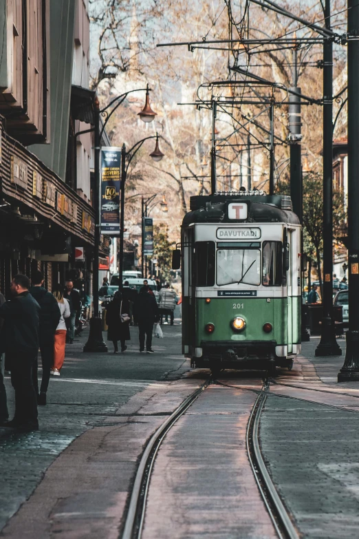 a green and white train traveling down a street, pexels contest winner, north melbourne street, 💋 💄 👠 👗, travelers walking the streets, prefecture streets