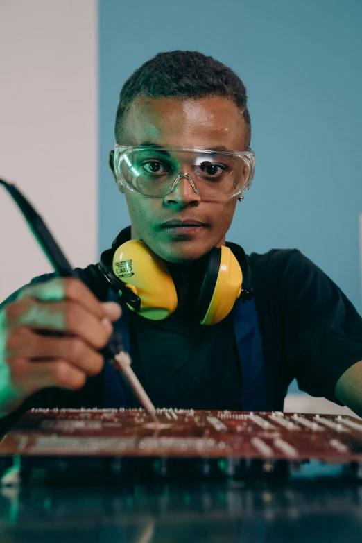 a man sitting at a table with a keyboard and headphones, inspired by Afewerk Tekle, with sparking circuits, maintenance, chemical woekshop, wearing goggles