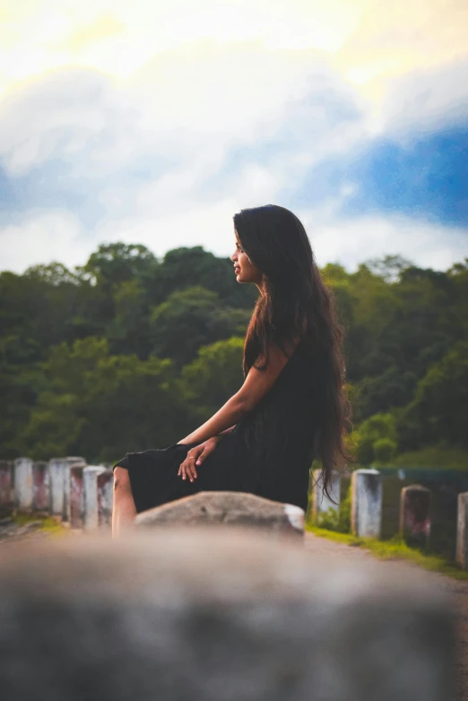 a woman sitting on top of a stone wall, by Max Dauthendey, pexels contest winner, romanticism, black long hair, assamese aesthetic, in a graveyard, panoramic view of girl