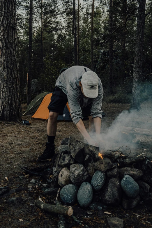 a man lighting a campfire in the woods, by Jaakko Mattila, unsplash contest winner, land art, bulky build, big rocks, grey, instagram story