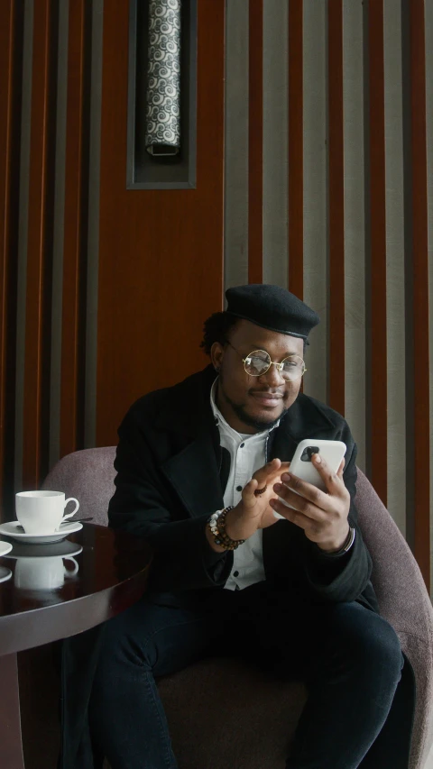 a man sitting in a chair looking at his cell phone, an album cover, inspired by Charles Martin, pexels, with square glasses, standing in a restaurant, portrait mode photo, gif