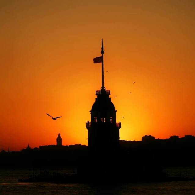 a large clock tower sitting on top of a body of water, by irakli nadar, pexels contest winner, hurufiyya, empire silhouette, ottoman sultan, the sun shines in, orange sky