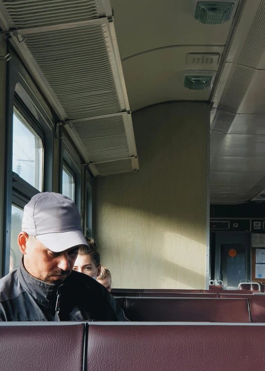 a man sitting on a train looking at his cell phone, by Jan Tengnagel, trending on unsplash, berets, in karuizawa, low quality photo, slightly sunny