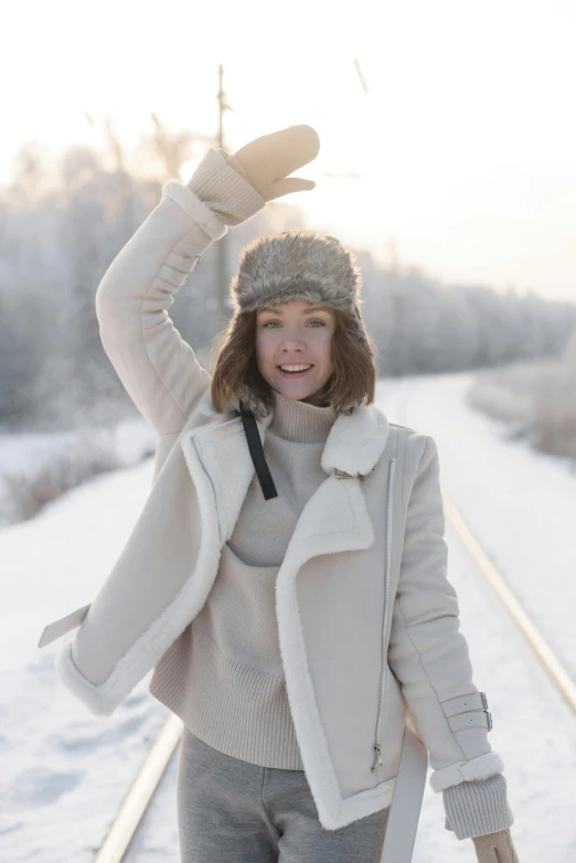 a woman standing on a train track in the snow, inspired by Louisa Matthíasdóttir, pexels contest winner, greeting hand on head, white hat, in an igloo, tan