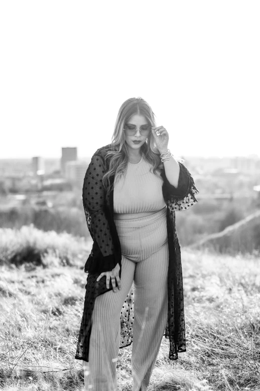 a pregnant woman wearing an all - white ensemble standing in the grass with her feet up