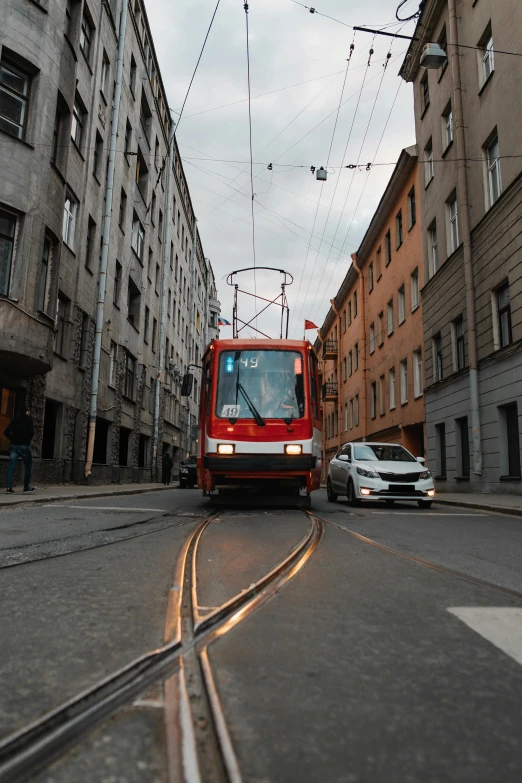 a red train traveling down a street next to tall buildings, pexels contest winner, kama russian electrocar, square, gif, electric cables