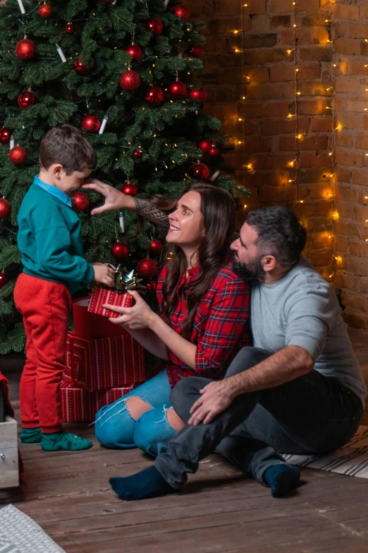 there is a woman holding a little boy that has a present under the christmas tree