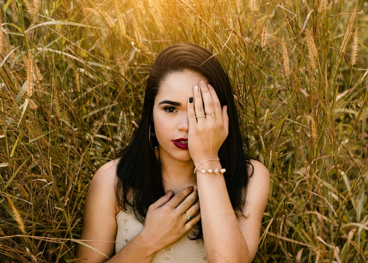 a woman holding her hands to her face in a field of tall grass, an album cover, inspired by Elsa Bleda, trending on pexels, renaissance, gold accessories, fair olive skin, girl with a pearl earringl, 15081959 21121991 01012000 4k