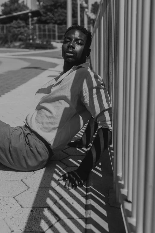 a black and white photo of a man sitting on a bench, dark skinned, soft and clear shadows, wearing pants and a t-shirt, lying on an abstract