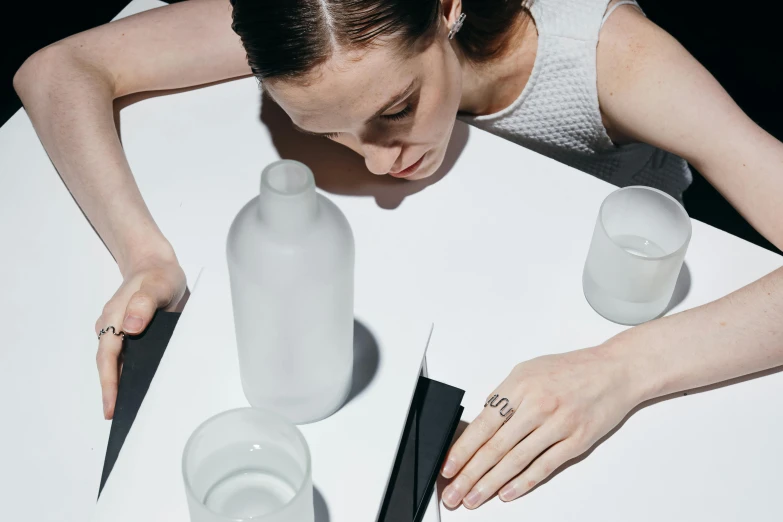a woman sitting at a table with a bottle of water, inspired by Marina Abramović, trending on unsplash, detail shot, silicone skin, sustainable materials, various posed
