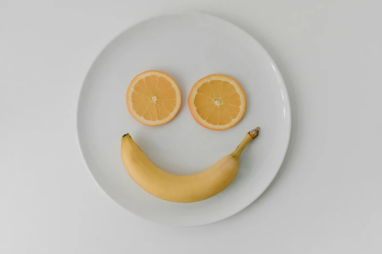 a white plate topped with sliced oranges and a banana, a picture, pexels, postminimalism, happy face, on a canva, made of glazed, smiling sweetly