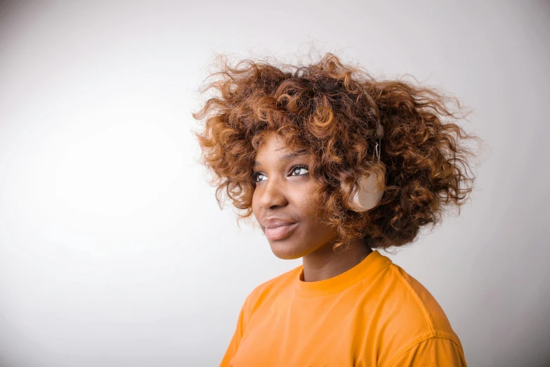 a close up of a person with an orange shirt, trending on pexels, afrofuturism, girl wearing headphones, curly brown hair, light-brown skin, casual pose