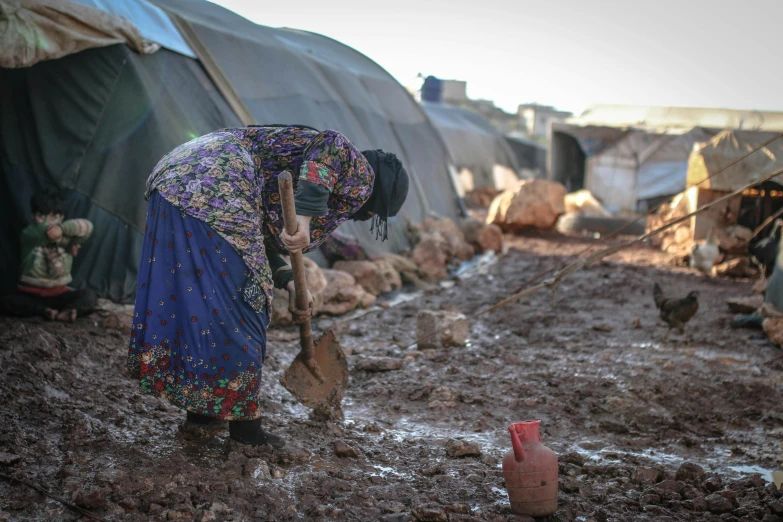 a woman digging in the mud with a shovel, hurufiyya, barrel fires and tents, multi - coloured, 💣 💥💣 💥, unedited