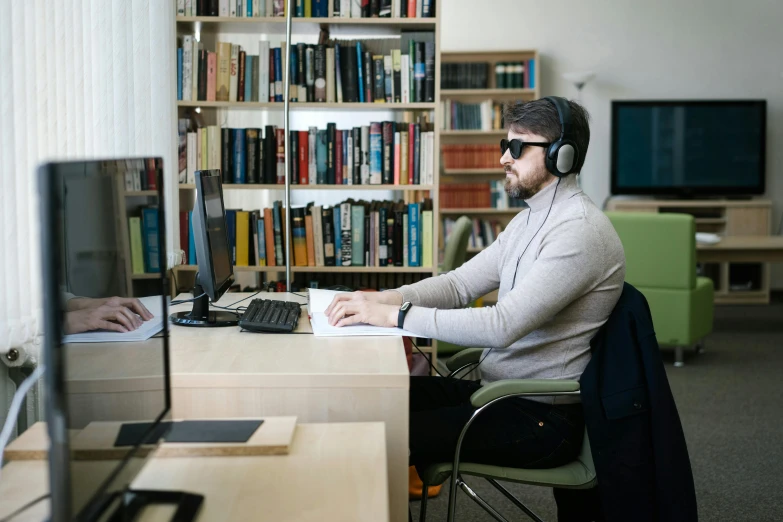 a man sitting at a desk in front of a computer, library nerd glasses, wearing modern headphone, luka mivsek, lachlan bailey