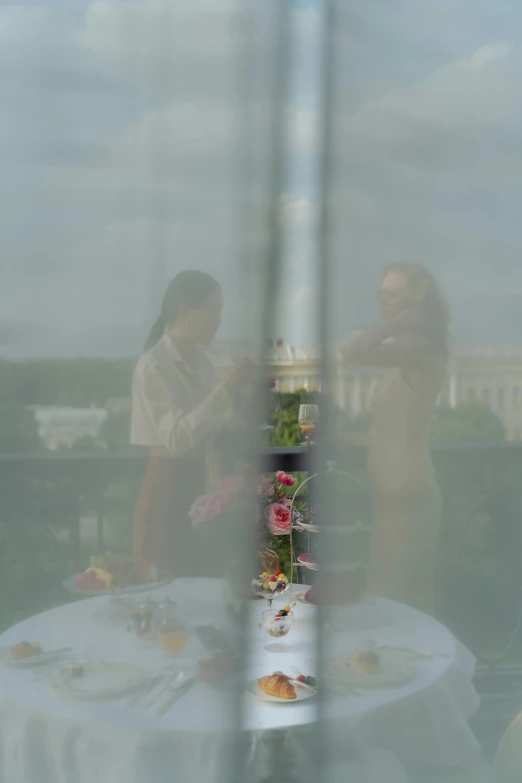 two women standing by an outdoor table near a window