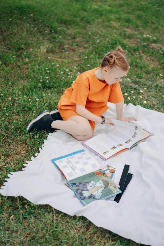 a little girl sitting on a blanket reading a book, inspired by Elsa Beskow, pexels contest winner, visual art, wearing an orange t shirt, girl wearing uniform, science magazines, handsome