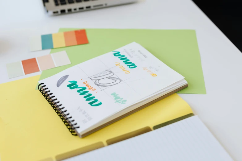 a notebook sitting on top of a desk next to a laptop, a child's drawing, inspired by Grillo Demo, unsplash, 9 9 designs, yellow and green scheme, close-up product photo, multi colour