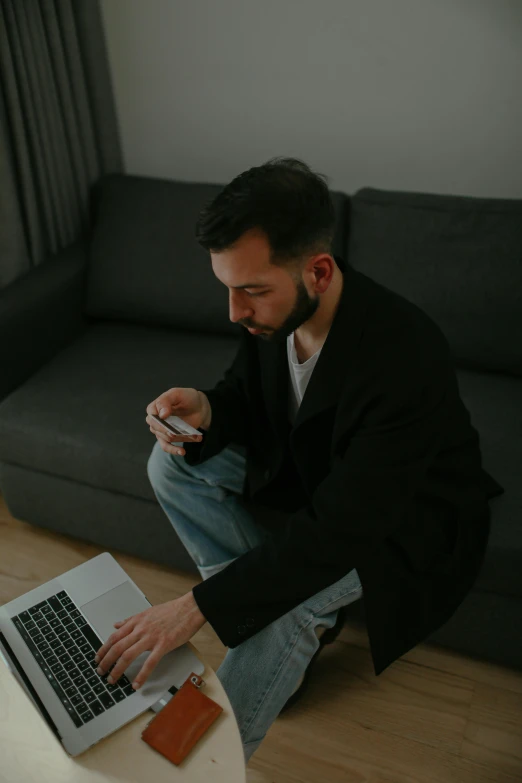 a man sitting on the floor using a laptop, a man wearing a black jacket, instagram picture, couch desk, taken in 2 0 2 0