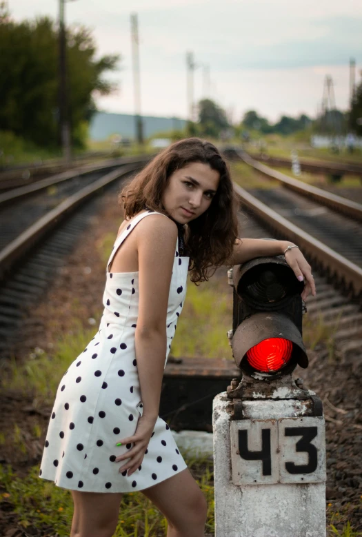 a woman in a polka dot dress standing next to a stop light, pexels contest winner, rail tracks, ukrainian girl, square, low quality photo