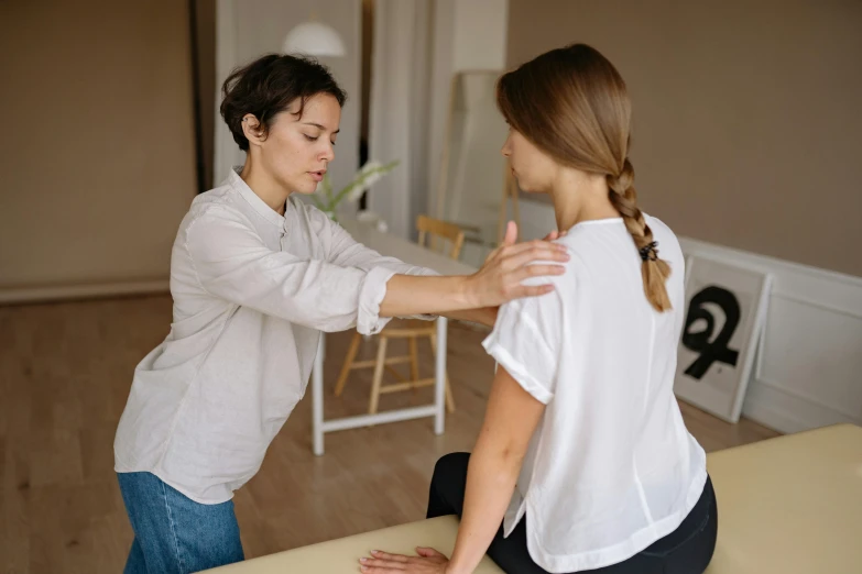 a woman sitting on top of a table next to a woman in a white shirt, by Adam Marczyński, trending on pexels, injured, bent - over posture, manuka, cast