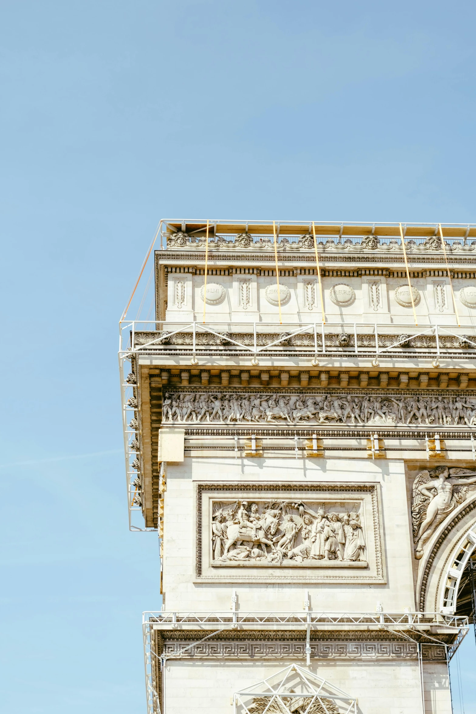 a clock that is on the side of a building, arc de triomphe full of graffiti, under construction, clear blue skies, jen atkin