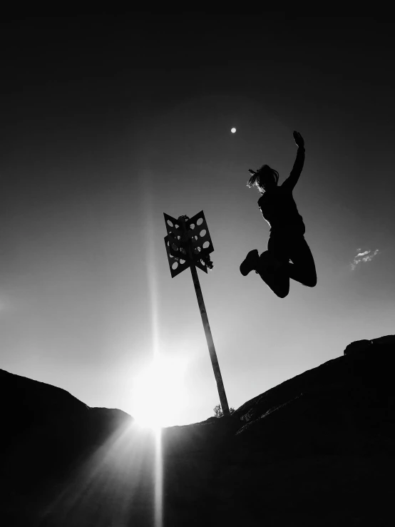 a black and white photo of a person jumping in the air, by Alexis Grimou, unsplash contest winner, selfie!!!!!, sun down, victorious on a hill, lights