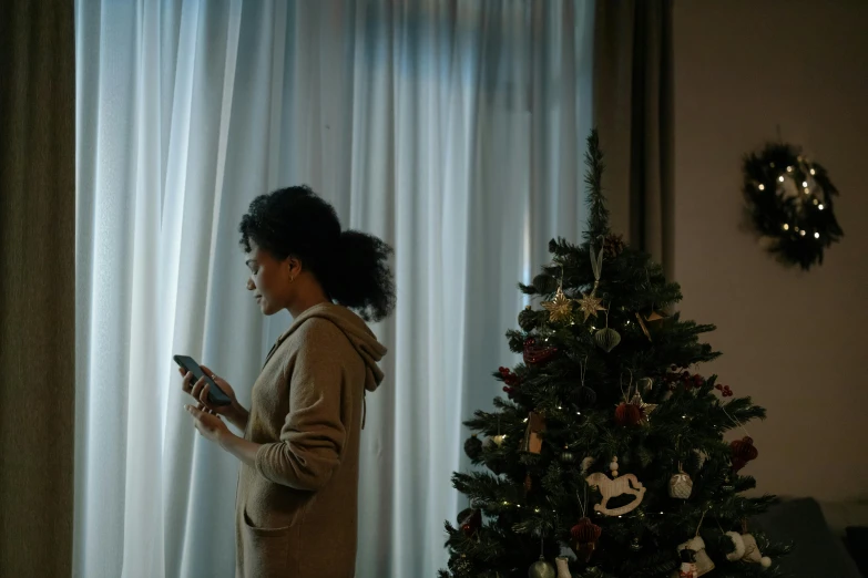 a woman looks at her cell phone in front of the christmas tree