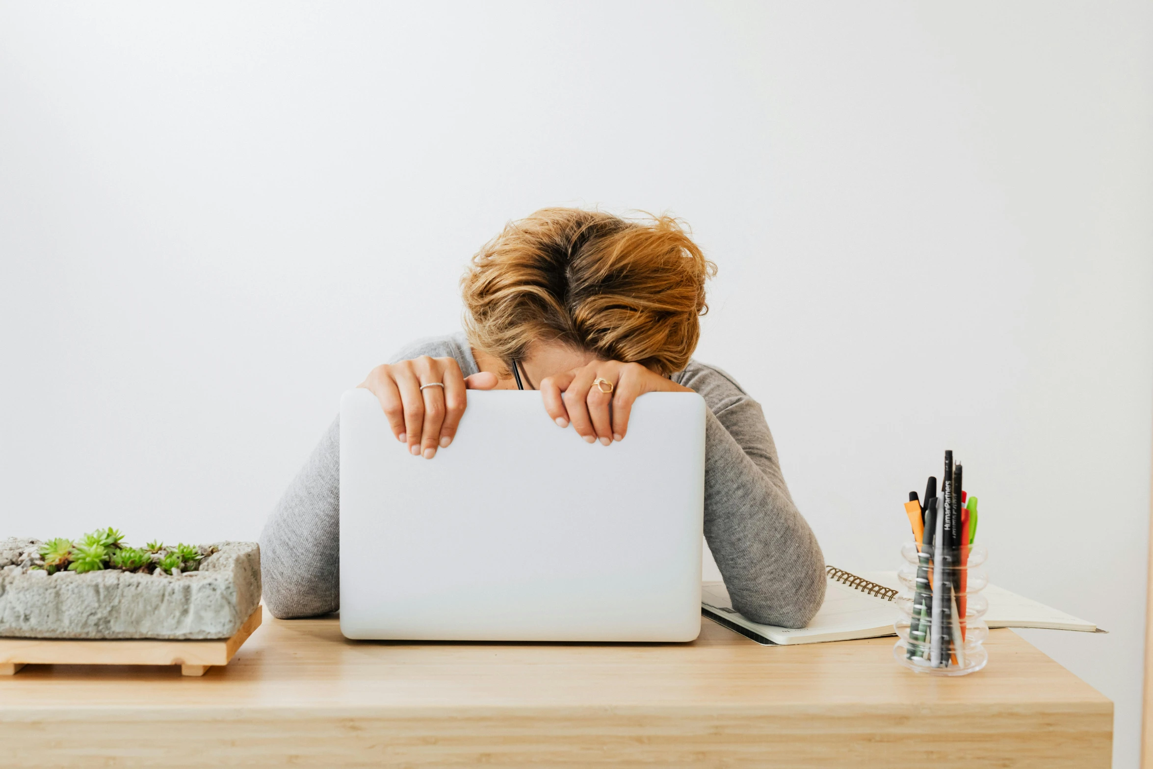 a woman sitting at a desk with a laptop in front of her, by Julia Pishtar, pexels, two exhausted, with a white background, head down, instagram post