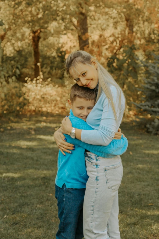 a woman hugging a boy while standing on the grass