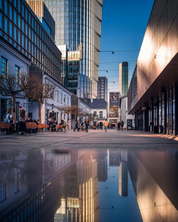 a puddle of water in the middle of a city street, a picture, by Tobias Stimmer, pexels contest winner, highrise business district, thumbnail, high definition photo, nice afternoon lighting