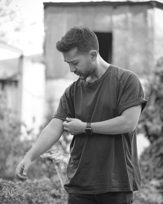 a black and white photo of a man looking at his watch, a black and white photo, sumatraism, ismail inceoglu and ruan jia, faded and dusty, casual pose, in the garden