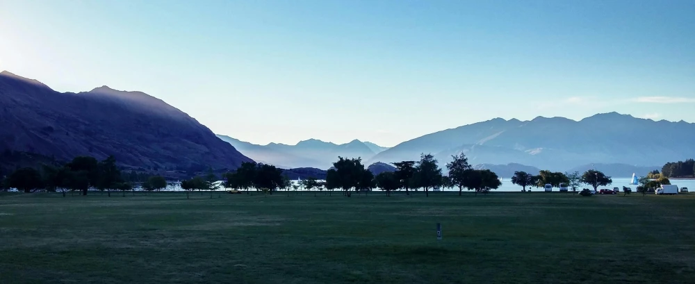 a man flying a kite on top of a lush green field, a picture, by Sophie Pemberton, pexels contest winner, hurufiyya, lakeside mountains, at gentle dawn blue light, golf course, college