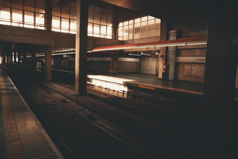 a train pulling into a train station next to a platform, a picture, inspired by Elsa Bleda, unsplash, brutalism, brown atmospheric lighting, factory floor, empty stage, 2000s photo