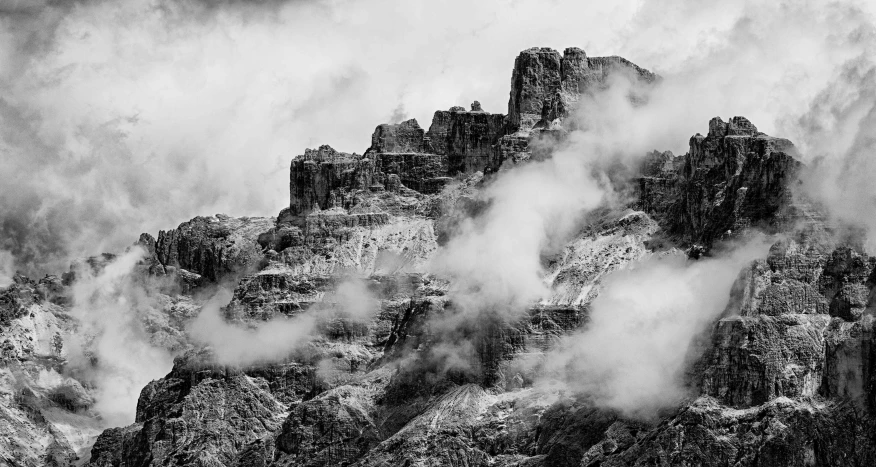 the tops of mountains in black and white are covered by cloud