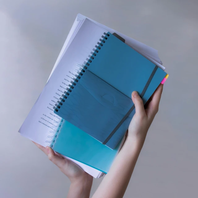 a person holding a notebook in their hands, aquamarine, coloured, reflective material, loose pages