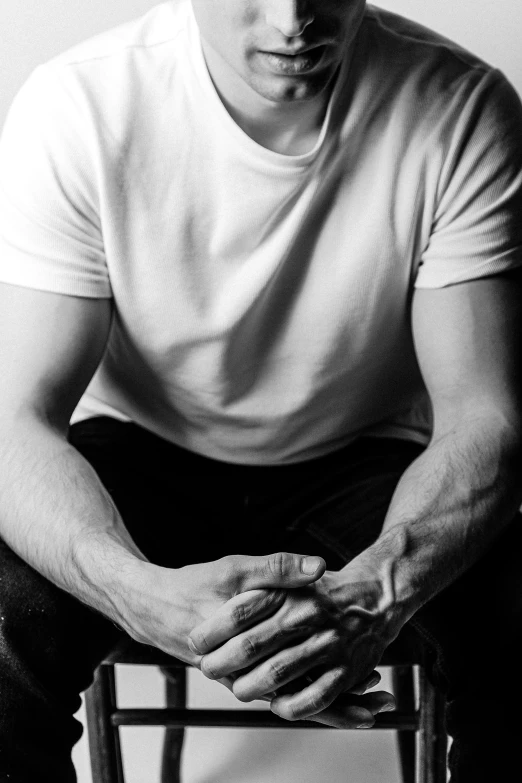 a black and white photo of a man sitting on a chair, a black and white photo, pexels, man in white t - shirt, closeup of arms, muscles, uploaded