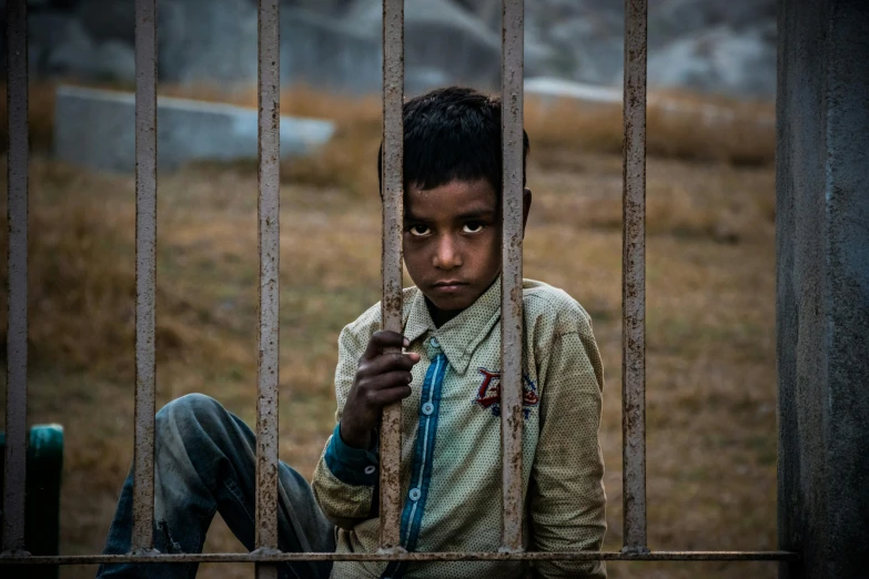 a young boy sitting behind a metal fence, by Ibrahim Kodra, pexels contest winner, realism, nepal, in jail, coloured photo, hd wallpaper