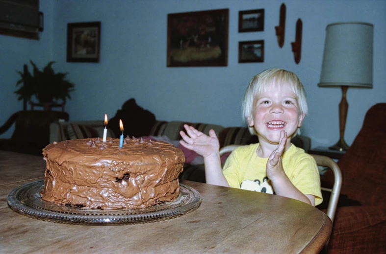 a little boy that is sitting in front of a cake, an album cover, pexels, hyperrealism, 1999 photograph, chocolate frosting, excited, stephen shore