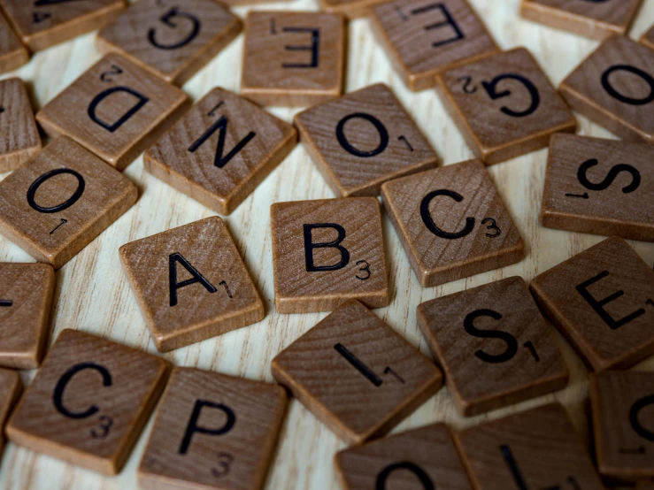 a pile of scrabbles sitting on top of a wooden table, unsplash, letterism, brown, fan favorite, alphabet soup, close - ups