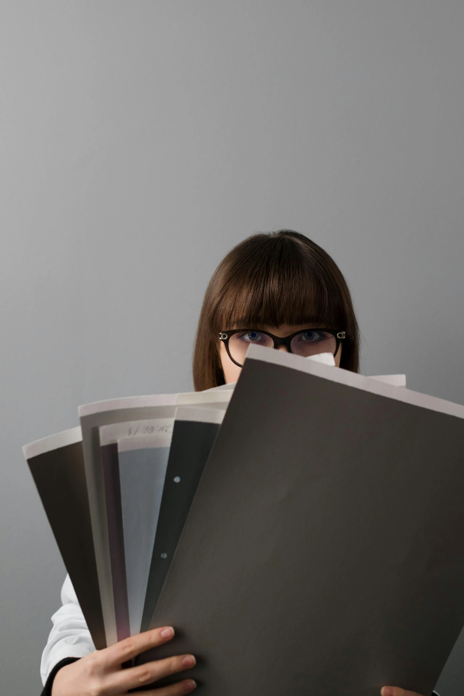 a woman holding a bunch of folders in front of her face, inspired by Zhang Kechun, unsplash, big glasses, getty images, rebecca sugar, xerography